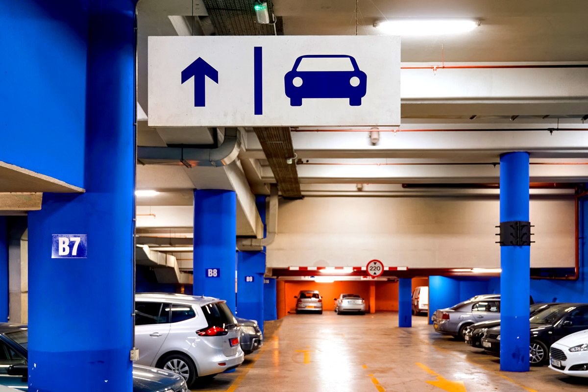 Parkhaus mit mehreren S&auml;ulen, einigen geparkten Autos und einem Schild mit Pfeil nach oben und Autosymbol