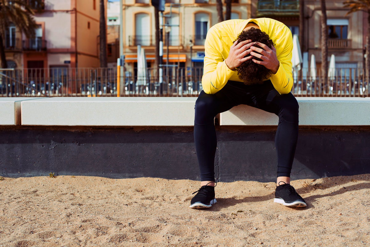 Eine Person sitzt auf einer Bank an einer Strandprommenade und hält den Kopf in den Händen.