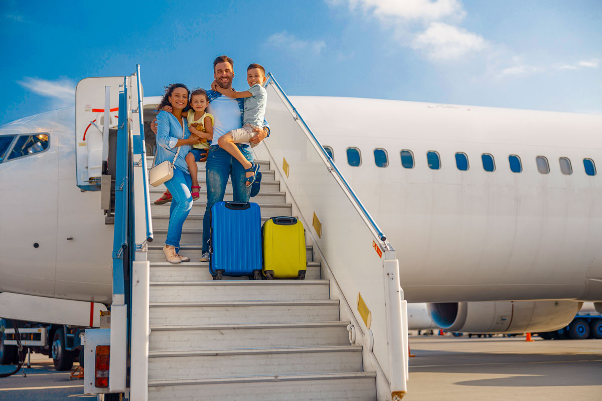 Familie mit zwei Kindern steht auf Flugzeugtreppe vor Passagierflugzeug mit zwei Koffern