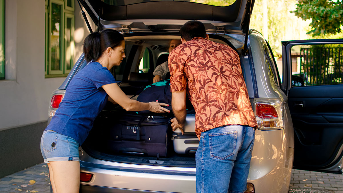 Zwei Personen laden Koffer in den geöffneten Kofferraum eines Autos
