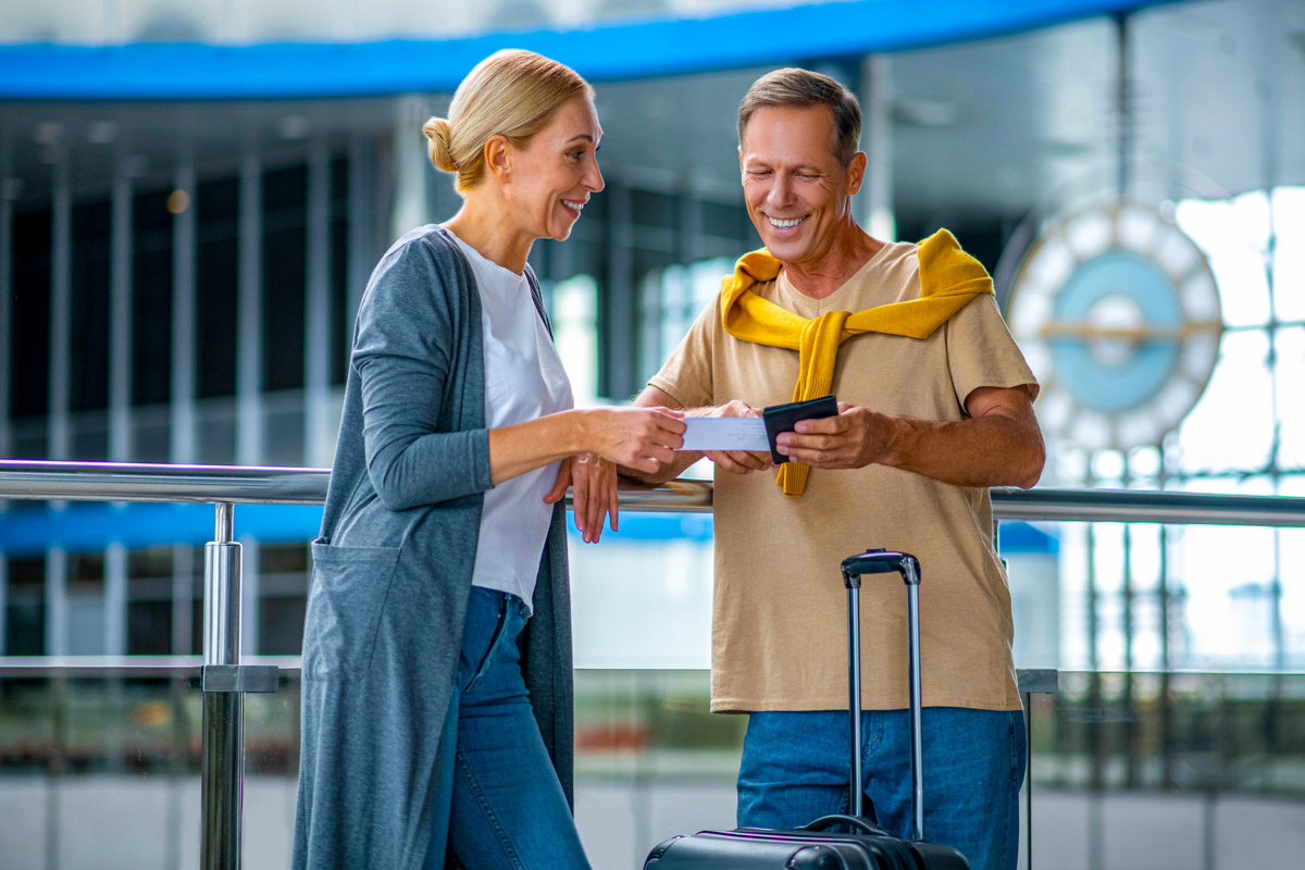 Ein Paar am Flughafen mit Koffer, die gemeinsam auf ein Smartphone schauen und lächeln