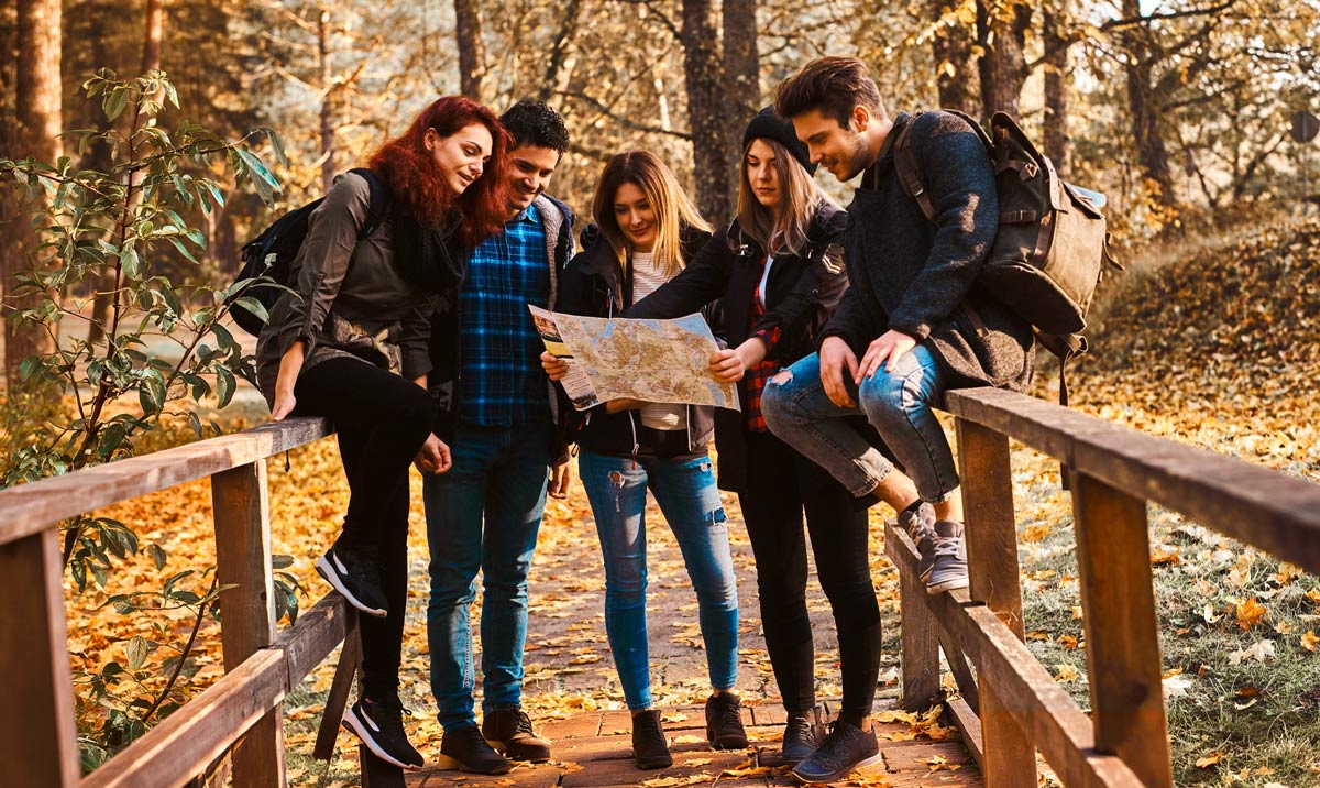 Fünf junge Erwachsene stehen bei herbstlichem Wetterauf einer Holzbrücke im Wald und betrachten gemeinsam eine Landkarte.