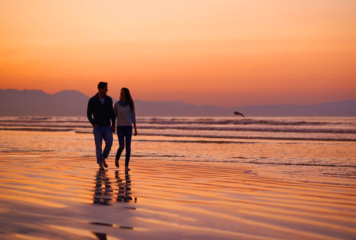 Paar geht am Strand bei Sonnenuntergang mit Bergen im Hintergrund